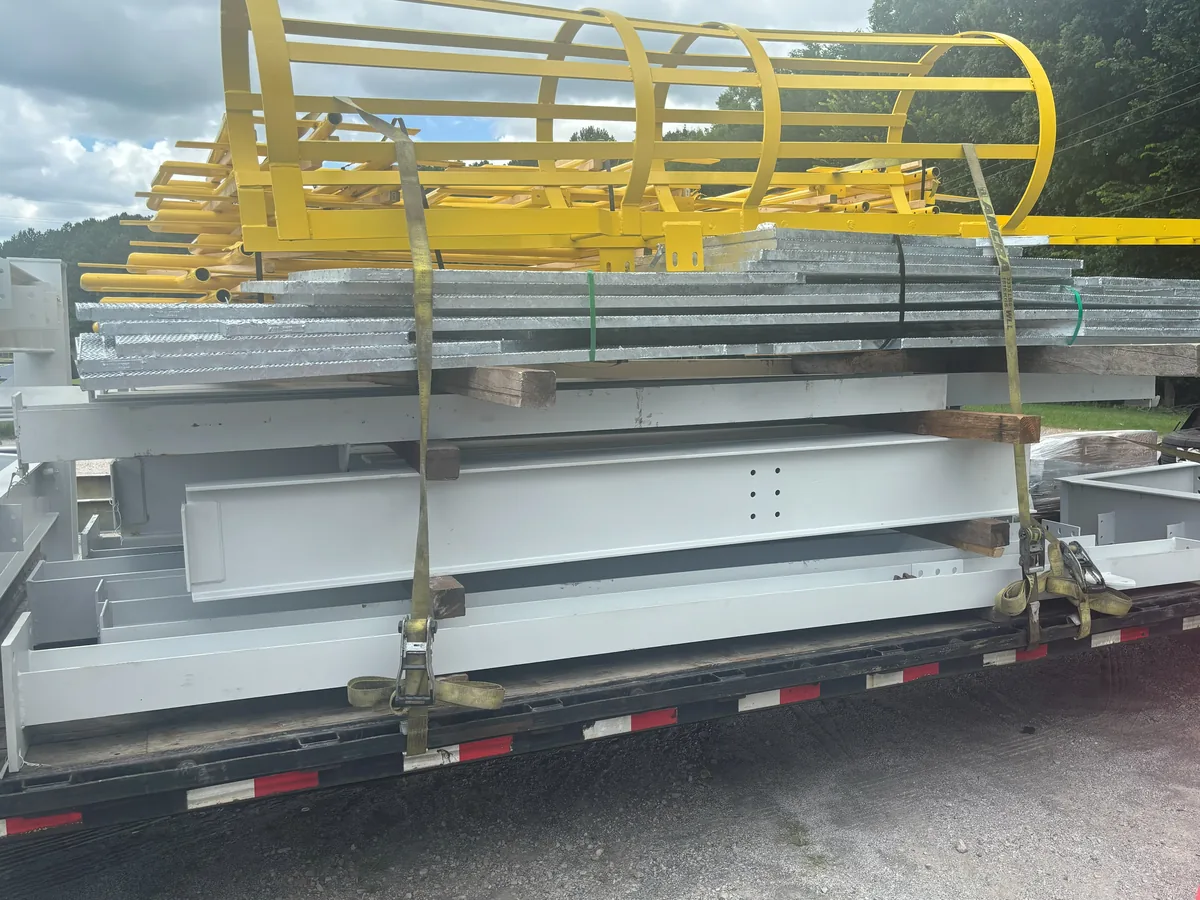 Galvanized grating, framing and a yellow ladder cage strapped down on a trailer