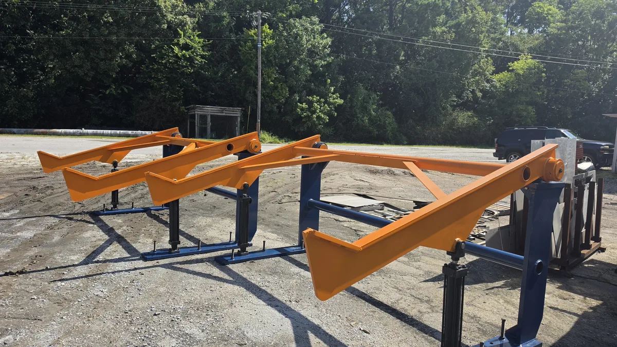 Painted lifting arms on their support stands in the fabrication yard