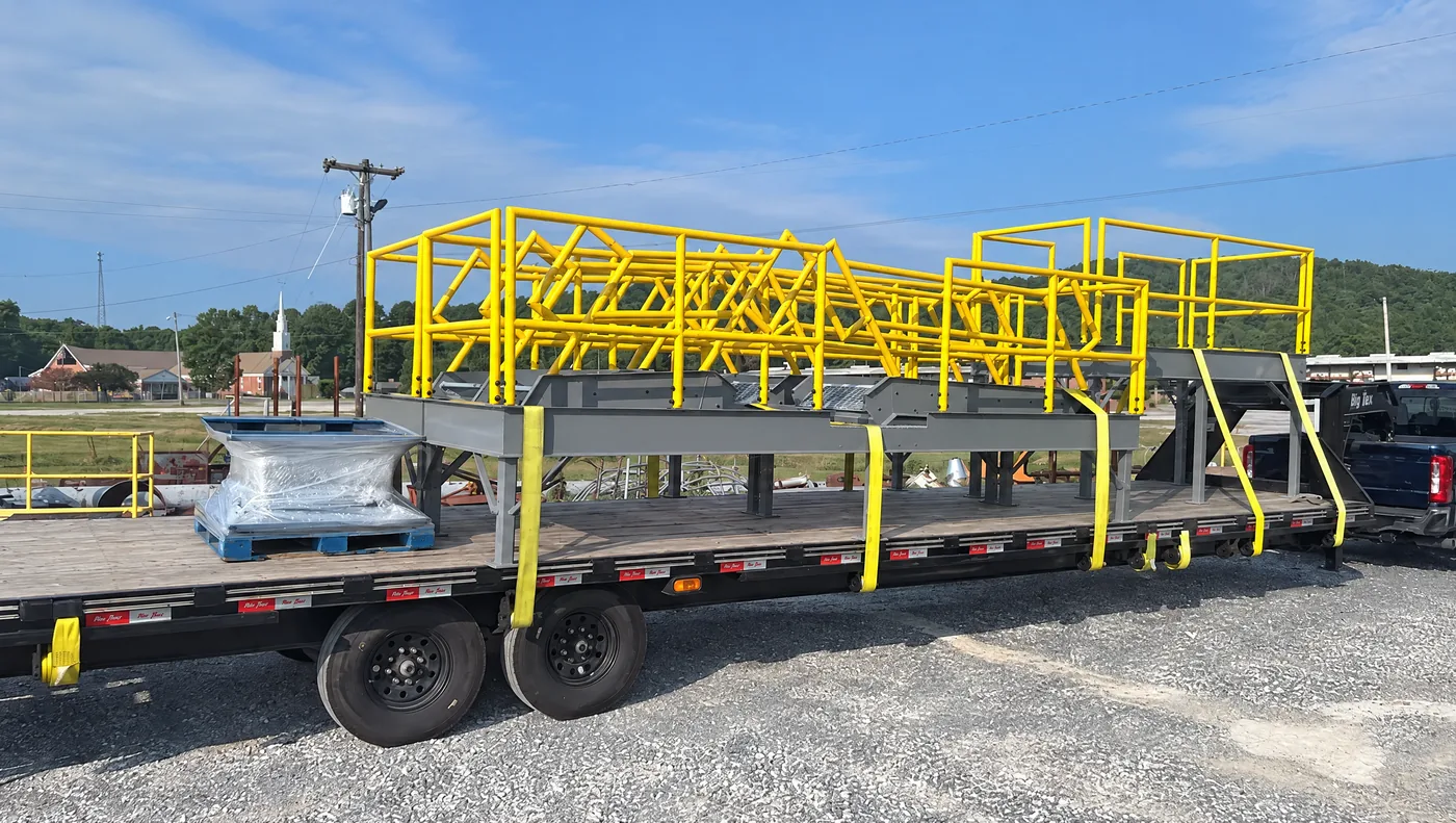 Steel access platform with yellow handrail strapped to a flatbed trailer, ready to ship