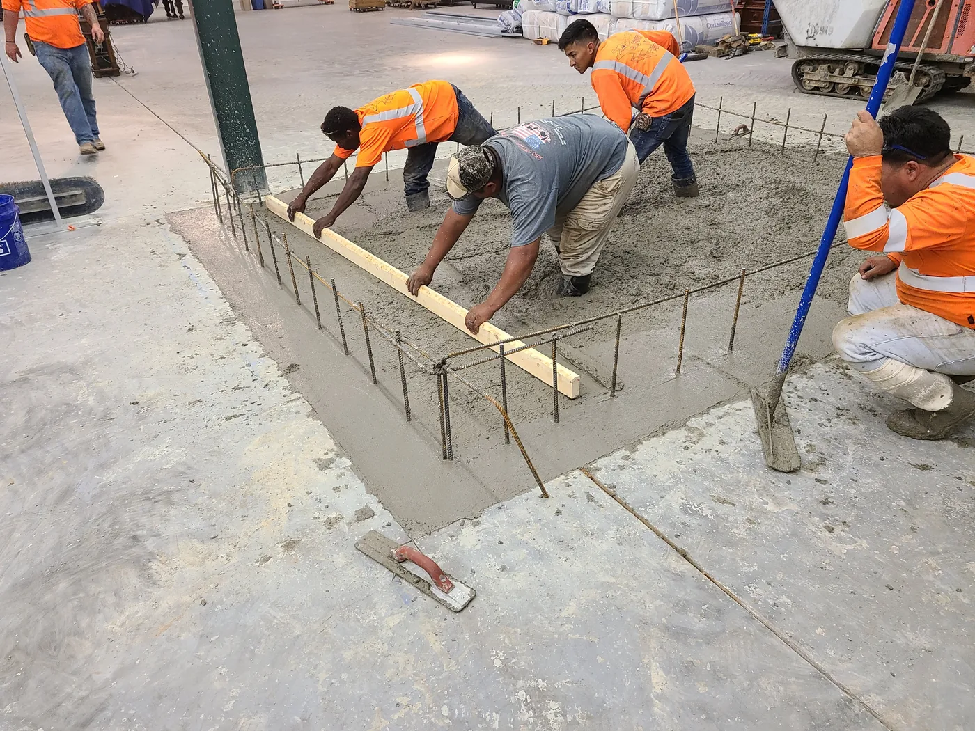 Three workers screeding a fresh concrete pour inside an equipment foundation